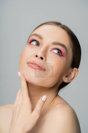 Photo for Portrait of joyful woman with pink eye shadow touching face isolated on grey - Royalty Free Image