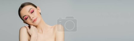 Junge Frau mit hellem Make-up berührt nackte Schulter isoliert auf grau, Banner 