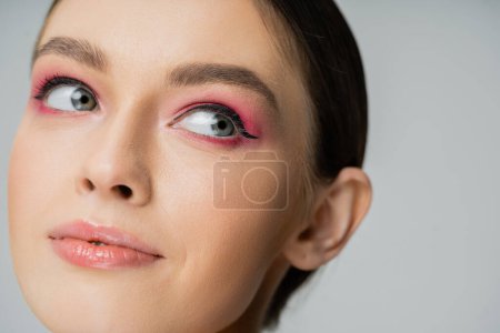 Nahaufnahme einer Frau mit rosa Lidschatten und Eyeliner isoliert auf grau 
