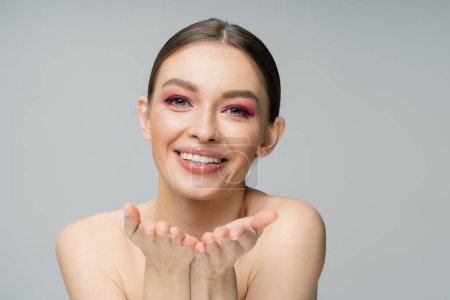 Positive junge Frau mit hellem Make-up zeigt vereinzelt auf graue Kamera 