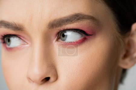 Foto de Vista recortada de una mujer joven con sombra de ojos rosados mirando hacia otro lado aislado en gris - Imagen libre de derechos