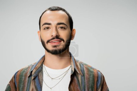Téléchargez les photos : Portrait de jeune homme barbu en chemise colorée souriant à la caméra isolé sur gris - en image libre de droit