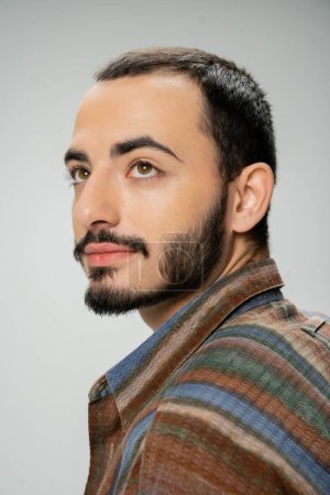 Téléchargez les photos : Portrait de bel homme barbu en chemise colorée regardant loin isolé sur gris - en image libre de droit