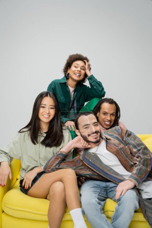 Photo for Happy african american woman looking away near multiethnic friends sitting on yellow sofa isolated on grey - Royalty Free Image
