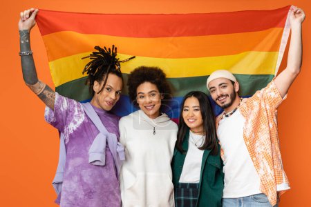 fröhlich und trendy multiethnische Freunde posieren mit lgbt Flagge isoliert auf orange