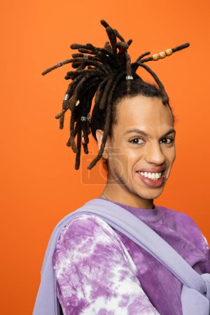Téléchargez les photos : Portrait of cheerful multiracial man with dreadlocks smiling at camera isolated on orange - en image libre de droit