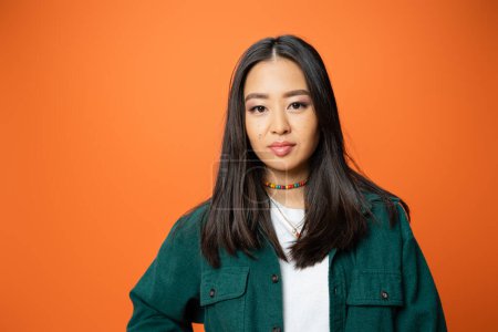 Téléchargez les photos : Portrait of brunette asian woman in green shirt and colorful beads isolated on orange - en image libre de droit