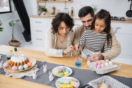 Family coloring Easter eggs near cake and cookies in kitchen 
