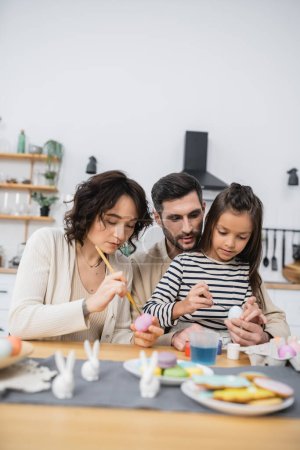 Family with daughter painting eggs during Easer at home 
