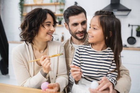 Smiling family with daughter coloring Easter eggs in kitchen 