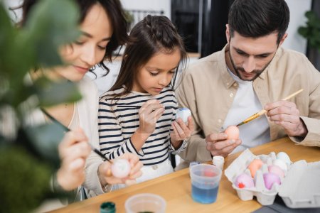 Téléchargez les photos : Child painting Easer egg near parents holding paintbrushes at home - en image libre de droit