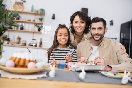 Lächelnde Familie blickt in die Kamera beim Färben von Ostereiern in der Küche 