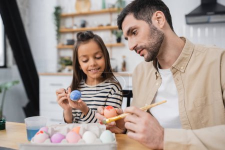 father and happy daughter coloring Easter eggs in kitchen  