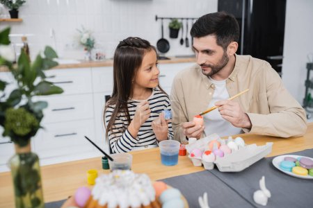 Téléchargez les photos : Homme parlant à sa fille tout en colorant les œufs de Pâques dans la cuisine - en image libre de droit
