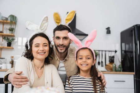 Positive Familie mit Oster-Stirnbändern blickt in Küche in die Kamera 