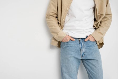 Cropped view of man in shirt holding hands in pockets of jeans on white background 