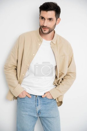 Bearded man in shirt and jeans posing on white background 