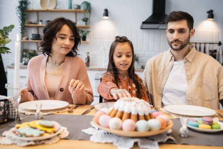 Family sitting near Easter dinner and candle on table at home 