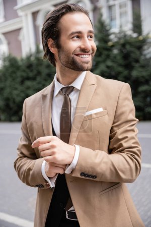 cheerful groom in beige formal wear adjusting sleeve on shirt 