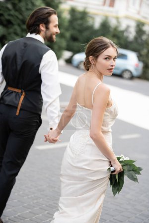 Bräutigam hält Hand der hinreißenden Braut im Brautkleid mit Blumenstrauß 