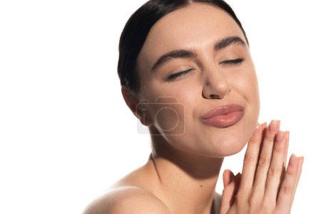 fröhliche junge Frau mit natürlichem Make-up und geschlossenen Augen schmollen Lippen isoliert auf weiß