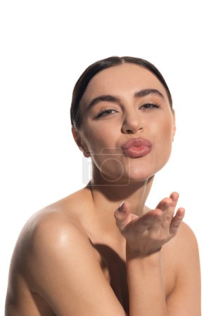 Téléchargez les photos : Gaie jeune femme avec maquillage naturel boudant lèvres tout en envoyant baiser d'air isolé sur blanc - en image libre de droit