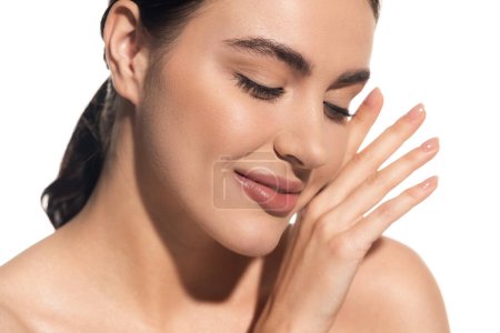 Téléchargez les photos : Jeune femme satisfaite avec maquillage naturel toucher doucement visage isolé sur blanc - en image libre de droit