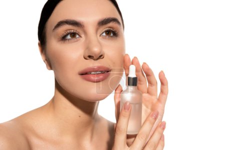 dreamy woman with bare shoulders holding bottle with moisturizing serum isolated on white 