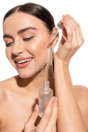 cheerful and brunette woman holding pipette with serum isolated on white 