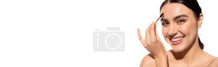 Téléchargez les photos : Femme heureuse et brune coiffant les sourcils avec pinceau et gel isolé sur blanc, bannière - en image libre de droit