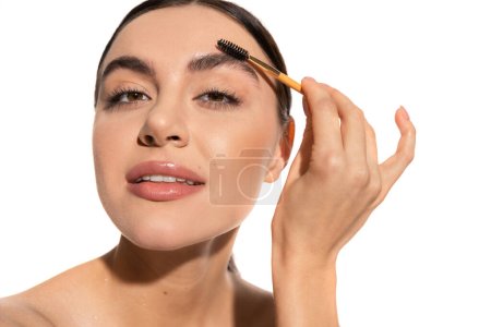 brunette woman styling eyebrows with brush and gel isolated on white 