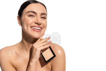smiling young woman with bare shoulders holding face powder isolated on white 