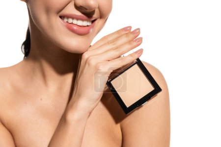 cropped view of happy young woman with bare shoulder holding neutral beige face powder isolated on white 