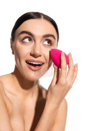 erstaunt junge Frau mit natürlichem Make-up hält rosa Schönheitsschwamm isoliert auf weiß 