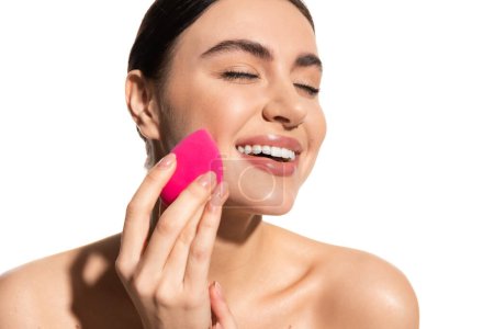 fröhliche junge Frau mit natürlichem Make-up hält rosa Schönheitsschwamm isoliert auf weiß 