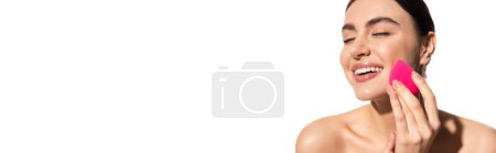 Téléchargez les photos : Joyeux jeune femme avec maquillage naturel tenant éponge de beauté rose isolé sur blanc, bannière - en image libre de droit