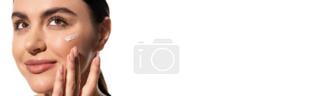close up view of young woman with face cream on cheek touching face isolated on white, banner 