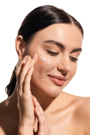 smiling woman applying moisturizing face cream on cheek isolated on white