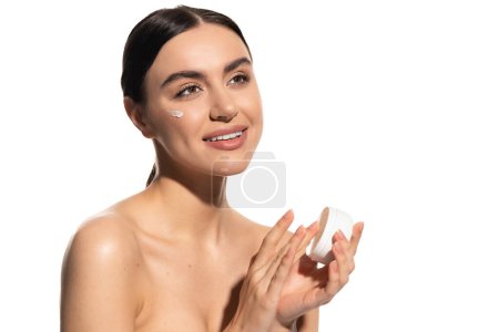 glückliche junge Frau mit nackten Schultern hält Glas mit feuchtigkeitsspendender Gesichtscreme isoliert auf weiß 