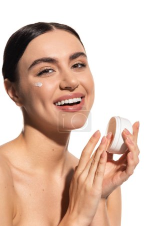 joyful woman with bare shoulders holding jar with moisturizing face cream isolated on white 