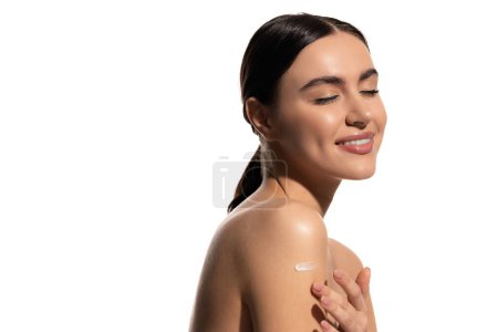 happy young woman with bare shoulders applying lotion on body isolated on white