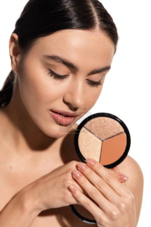 brunette young woman with bare shoulder holding bronzer and highlighter palette isolated on white 