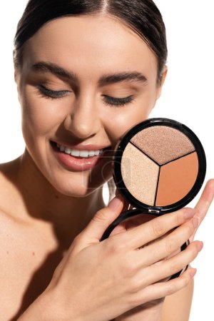cheerful young woman with bare shoulders holding bronzer and highlighter palette isolated on white 