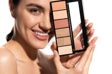 smiling young woman covering eye with eye shadow palette isolated on white 