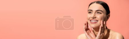 happy young woman with bare shoulders touching soft cheeks isolated on pink, banner 