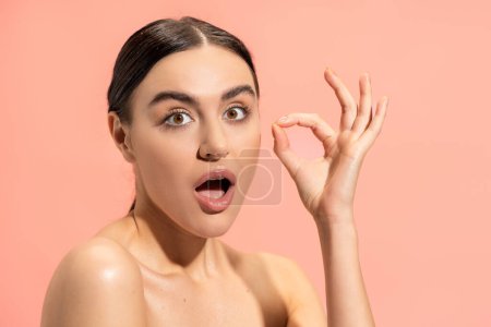 surprised woman with opened mouth showing ok sign isolated on pink 