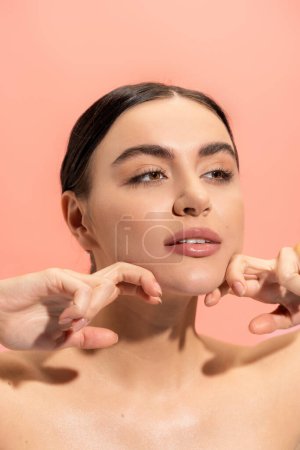 brunette jeune femme avec peau douce faire massage du visage isolé sur rose 