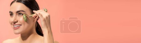 Photo for Happy young woman doing face massage with jade roller isolated on pink, banner - Royalty Free Image