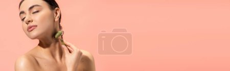 Photo for Brunette young woman doing neck massage with jade roller isolated on pink, banner - Royalty Free Image