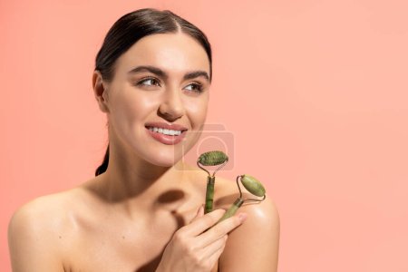 Photo for Happy young woman with bare shoulders holding jade rollers isolated on pink - Royalty Free Image